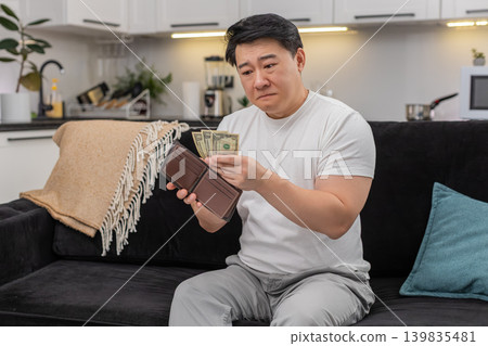 Asian man checks wallet sees only small dollar bills frowns and sets saving goal for budget plan new Asian man checks wallet sees only small dollar bills frowns and sets saving goal for budget plan new 139835481