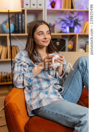 Young woman on home sofa enjoying hot drink and warming up in cozy living room during calm rest time Young woman on home sofa enjoying hot drink and warming up in cozy living room during calm rest time 139835496