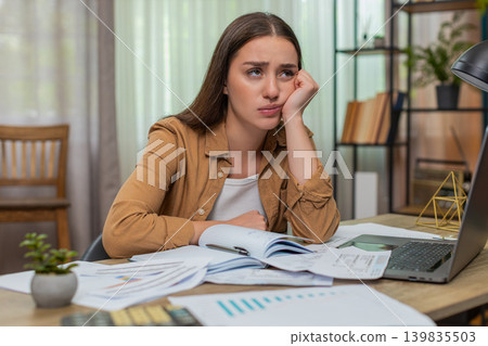 Young woman head in hands staring at overdue bills calculator and laptop wondering how she will pay Young woman head in hands staring at overdue bills calculator and laptop wondering how she will pay 139835503