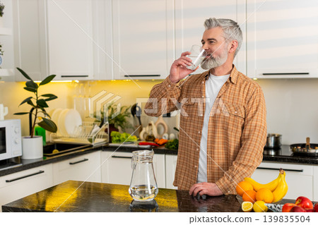 Middle-aged man drinking water in kitchen for healthy diet hydration weight loss lifestyle at home Middle-aged man drinking water in kitchen for healthy diet hydration weight loss lifestyle at home 139835504