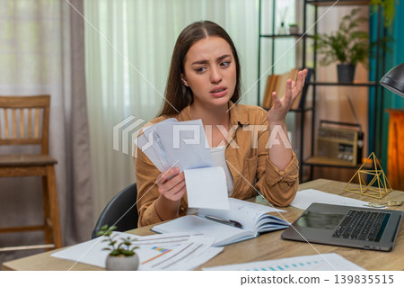 Young woman shocked by huge utility bill raises eyebrows then throws papers onto desk in disbelief 139835515