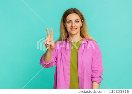 Woman showing peace sign with two fingers and smiling expressing positivity harmony and friendliness 139835516