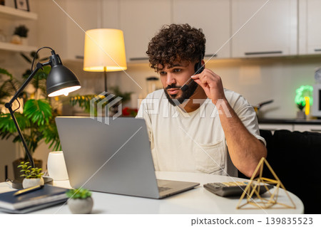 Arabian man with headset microphone assists client on hotline logs request polite service at night Arabian man with headset microphone assists client on hotline logs request polite service at night 139835523