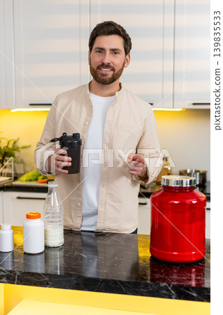 Middle-aged man mixing protein shake in kitchen smiling for fitness diet nutrition workout at home Middle-aged man mixing protein shake in kitchen smiling for fitness diet nutrition workout at home 139835533