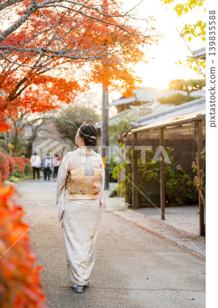 A woman in a kimono walks down a traditional street ablaze with autumn colors, seen from behind. Kyoto Prefecture, Japan. 139835588