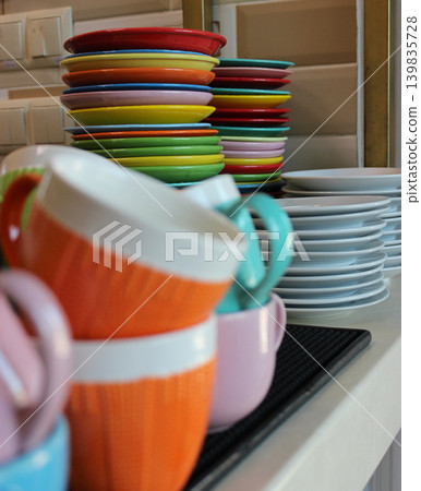 Kitchen table with stack of colorful plates behind the stack of defocused colored cups after holiday party  139835728