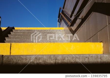Concrete stairs with bright yellow safety stripes in an urban environment. Low angle view showing metal railings, blue sky. Drection, urban structure. Concrete stairs with bright yellow safety stripes in an urban environment. Low angle view showing metal railings, blue sky. Drection, urban structure. 139835795