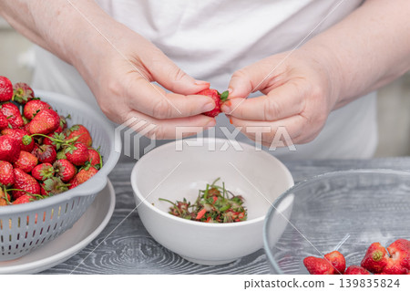 Women's hands brushing strawberries over a white bowl on a kitchen table Women's hands brushing strawberries over a white bowl on a kitchen table 139835824