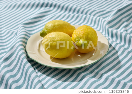 Fresh Lemons on a White Ceramic Plate on a Wrinkled Blue Striped Tablecloth. Front View Fresh Lemons on a White Ceramic Plate on a Wrinkled Blue Striped Tablecloth. Front View 139835846