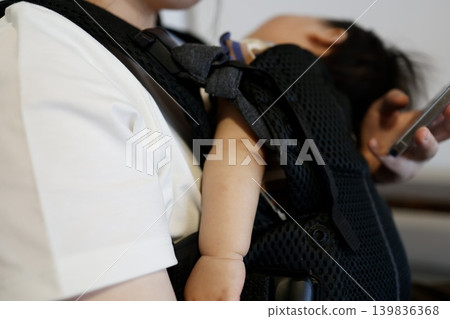 A baby sleeping in a baby carrier. Baby care: sleeping in the mother's arms. 139836368