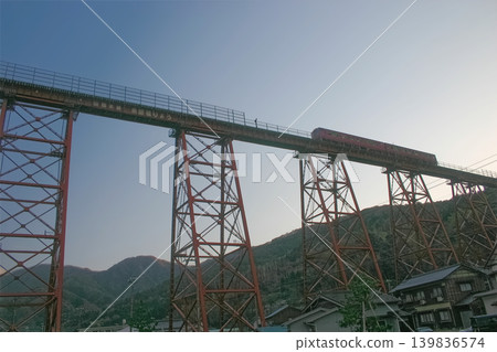 A restored shot of a diesel train crossing the former Amarube Railway Bridge (trestle bridge) in Kami Town, Hyogo Prefecture, against a sunset backdrop. A restored shot of a diesel train crossing the former Amarube Railway Bridge (trestle bridge) in Kami Town, Hyogo Prefecture, against a sunset backdrop. 139836574