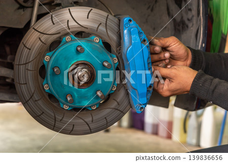 Mechanic installing performance brake caliper on car drilled brake rotor automotive maintenance repair service vehicle safety inspection Mechanic installing performance brake caliper on car drilled brake rotor automotive maintenance repair service vehicle safety inspection 139836656