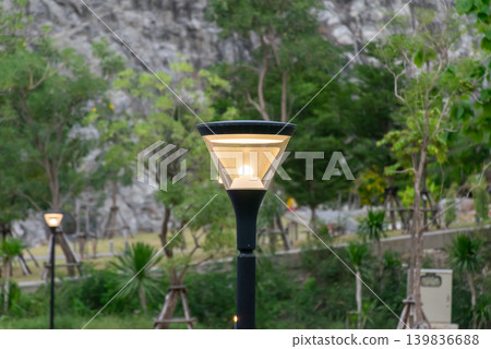 Illuminated outdoor garden lamp surrounded by trees greenery creating peaceful landscape lighting in natural park setting Illuminated outdoor garden lamp surrounded by trees greenery creating peaceful landscape lighting in natural park setting 139836688