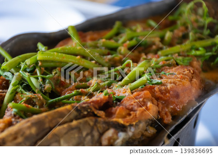 Traditional spicy fish dish topped fresh greens served hot rich seasoning savory flavors in closeup view Traditional spicy fish dish topped fresh greens served hot rich seasoning savory flavors in closeup view 139836695