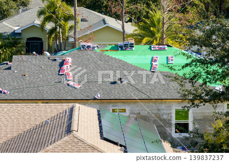 Asphalt shingles being applied to new home rooftop. Roofing workers securing shingles. Florida residential construction site. Asphalt shingles being applied to new home rooftop. Roofing workers securing shingles. Florida residential construction site. 139837237
