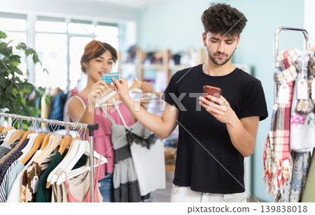 Bored husband scrolls down phone and hands his wife credit card to pay for purchases 139838018