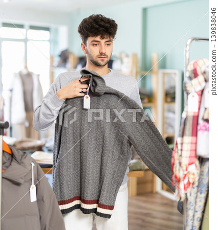 Young man chooses sweater in clothing store Young man chooses sweater in clothing store 139838046