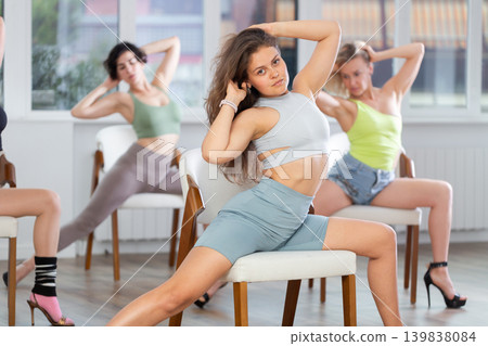 Girl performing sensual burlesque dance on chair during group class Girl performing sensual burlesque dance on chair during group class 139838084