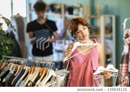 Young woman chooses dresses and tops in store Young woman chooses dresses and tops in store 139838138