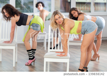 Group of women in high heels rehearsing dance while leaning on chair Group of women in high heels rehearsing dance while leaning on chair 139838142