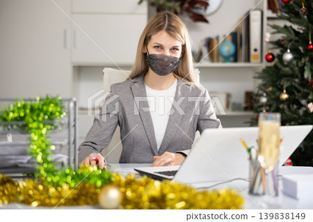 Portrait of young woman office worker in mask in Christmas decorated office Portrait of young woman office worker in mask in Christmas decorated office 139838149