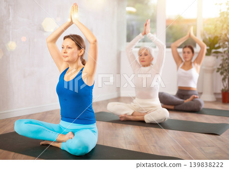 Woman sitting in Padmasana position with hands in namaste above head Woman sitting in Padmasana position with hands in namaste above head 139838222