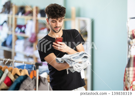 While shopping, guy scans barcode on label of jeans While shopping, guy scans barcode on label of jeans 139838319