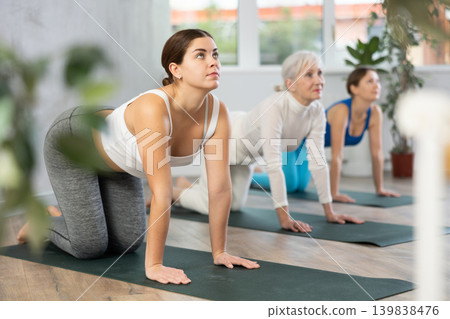 Woman doing yoga with group in fitness studio, standing in stretching asana Mukha Shvanasana Woman doing yoga with group in fitness studio, standing in stretching asana Mukha Shvanasana 139838476