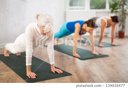Diligent women practicing plank pose of yoga in light fitness room Diligent women practicing plank pose of yoga in light fitness room 139838477