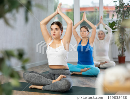 Active women practice pose sitting cross-legged with their arms raised Active women practice pose sitting cross-legged with their arms raised 139838488