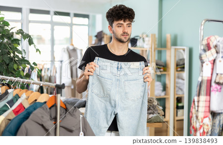 Regular customer guy chooses color and style of jeans trousers Regular customer guy chooses color and style of jeans trousers 139838493