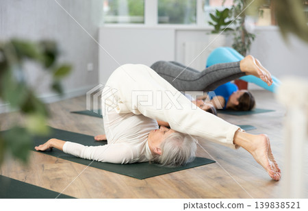 Elderly woman doing Halasana asana during group yoga training Elderly woman doing Halasana asana during group yoga training 139838521