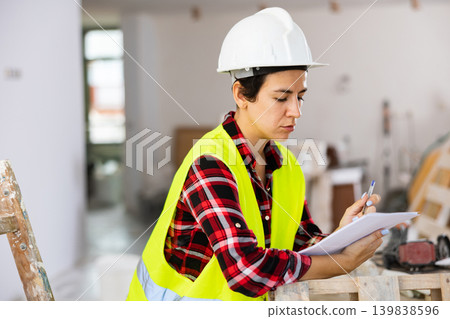 Female architect with papers in hands taking notes in building under renovation Female architect with papers in hands taking notes in building under renovation 139838596