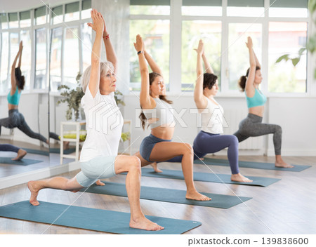 Woman performing revolved side angle pose Parivrtta Parsvakonasana during yoga class with female group in fitness studio Woman performing revolved side angle pose Parivrtta Parsvakonasana during yoga class with female group in fitness studio 139838600