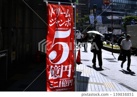The dream door to Tokyo's urban landscape... A banner advertising the 500 million yen Dream Jumbo lottery sways in the wind. Businessmen walk with their heads down... = Shibuya 139838851