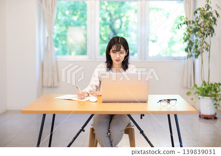 A young Japanese woman taking notes in a notebook while working on her computer. 139839031