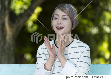 幾位老年婦女坐在綠樹環繞的公園長椅上觀看體育比賽。 139839315