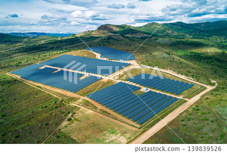 Hundreds of blue solar panels stretch across a large green field under natural light Hundreds of blue solar panels stretch across a large green field under natural light 139839526