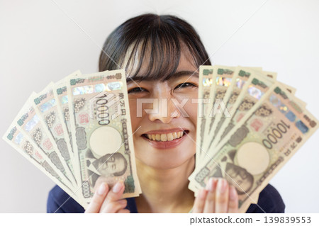 一位年輕的日本女子麵帶微笑，攤開十張面值10000日元的鈔票。 139839553