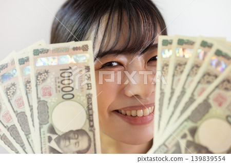 一位年輕的日本女子麵帶微笑，攤開十張面值10000日元的鈔票。 139839554
