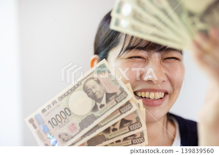 一位年輕的日本女子麵帶微笑，攤開十張面值10000日元的鈔票。 139839560