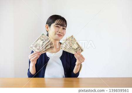 一位年輕的日本女子麵帶微笑，攤開十張面值10000日元的鈔票。 139839561