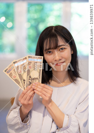 A young Japanese woman smiles, holding three 10,000 yen bills. A young Japanese woman smiles, holding three 10,000 yen bills. 139839971