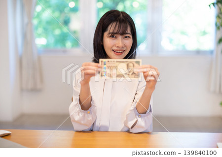 A young Japanese woman smiles, holding a 10,000 yen bill. A young Japanese woman smiles, holding a 10,000 yen bill. 139840100