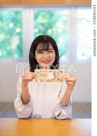 A young Japanese woman smiles, holding a 10,000 yen bill. A young Japanese woman smiles, holding a 10,000 yen bill. 139840101