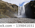 Stunning waterfall cascades down rocky cliffs, surrounded by lush greenery and rainbow in mist 139841031
