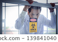 Scientist laboratory window warning danger covid biohazard pandemic safety quarantine Scientist laboratory looking through window covid biohazard 139841040