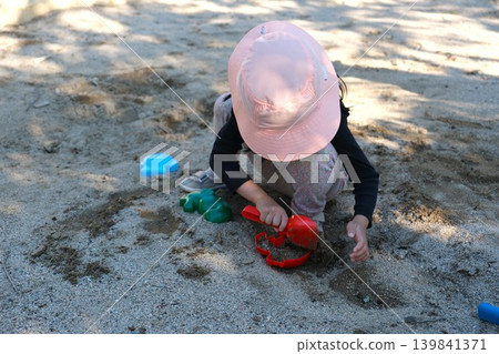 A child filling a red sand mold with sand in the sandbox. A child filling a red sand mold with sand in the sandbox. 139841371