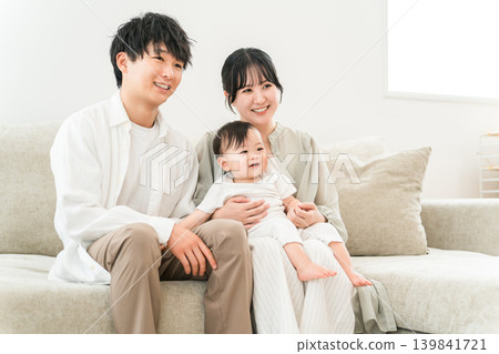 A young family sitting on a sofa and holding a baby, parent and child, family (childcare support, measures to combat declining birthrate) A young family sitting on a sofa and holding a baby, parent and child, family (childcare support, measures to combat declining birthrate) 139841721