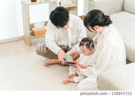A family of parenting generation reading a picture book to their child or baby in the living room of their home (childcare, parenting, skinship) A family of parenting generation reading a picture book to their child or baby in the living room of their home (childcare, parenting, skinship) 139841723